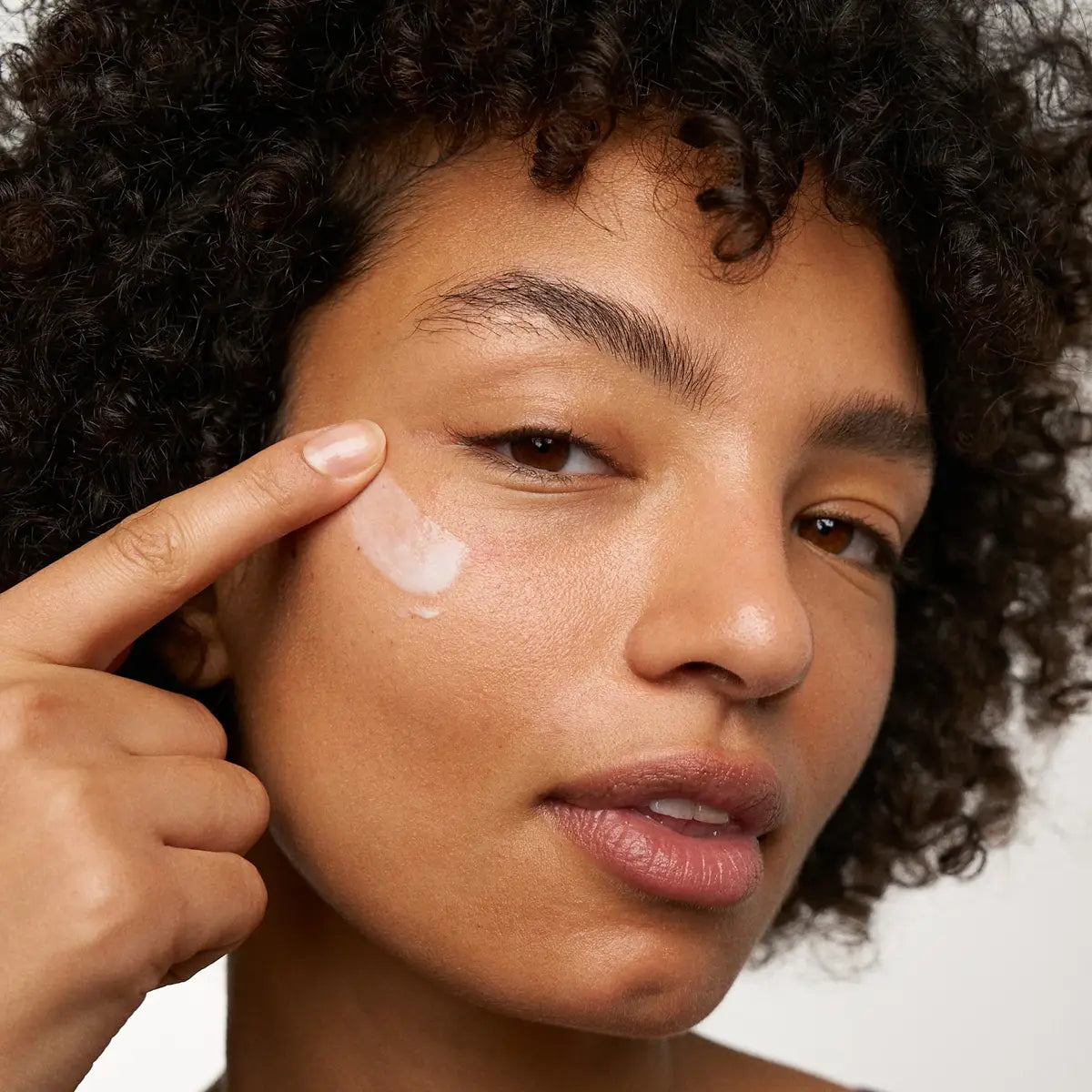 Woman applying cream to her face with a neutral background