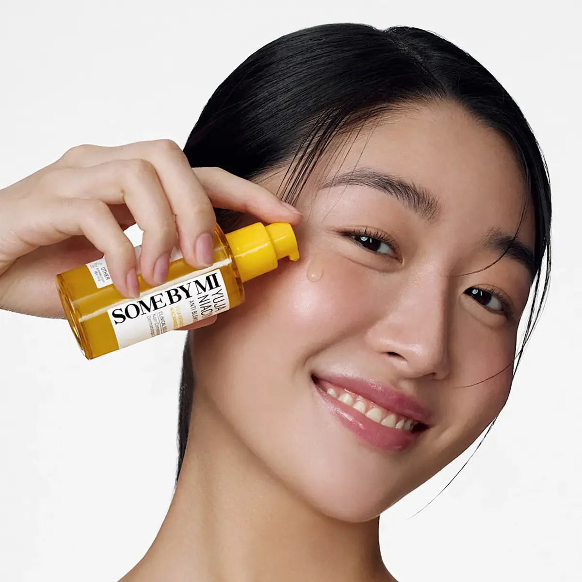 Model holding SOME BY MI Yuja Niacin Anti-Blemish Serum 50mL, showcasing bright, clear skin.