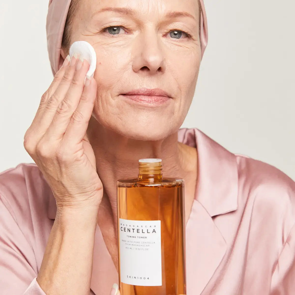 Woman applying a product to her face with a bottle of Centella Asiatica in front of her.
