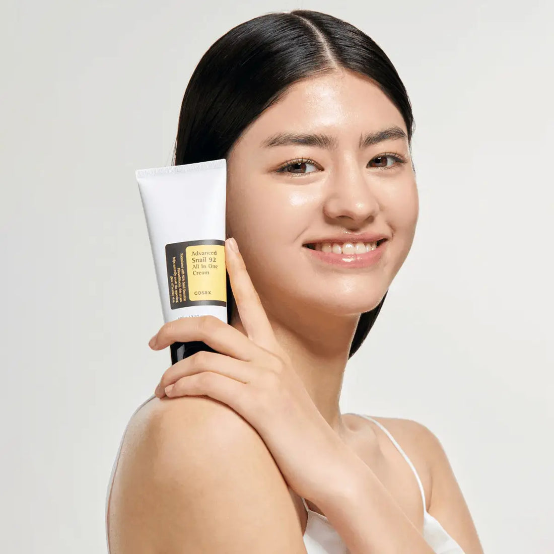 Woman holding a Cosrx Advanced Snail 92 All in One Cream with a plain background