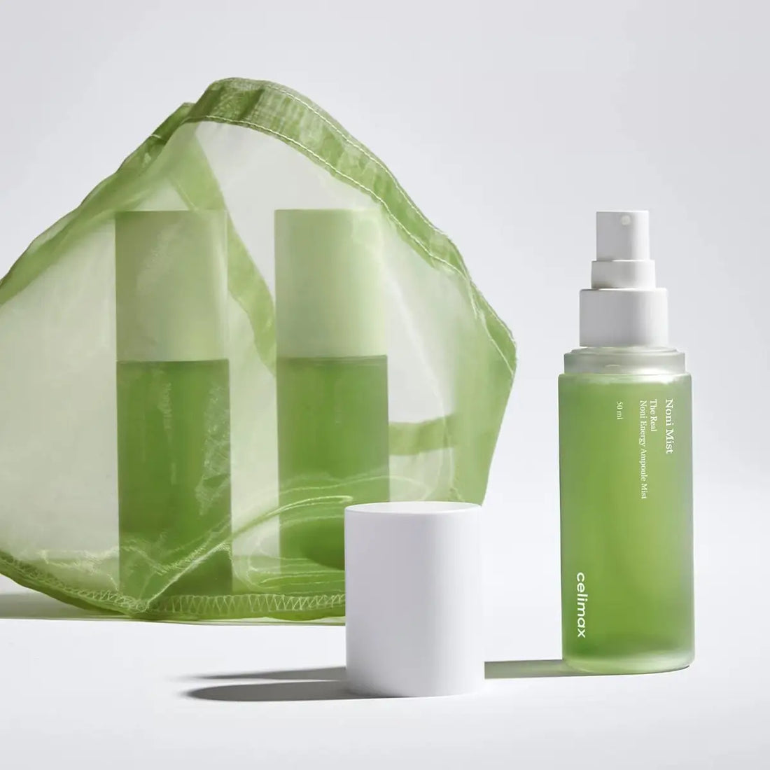 Skincare products including a green bottle, white container, and green mesh bag on a light gray background.