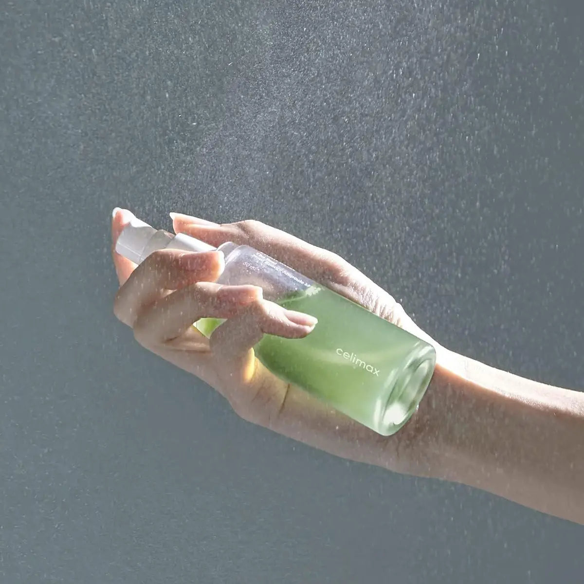 Hand holding a green bottle labeled 'colimax' against a gray background