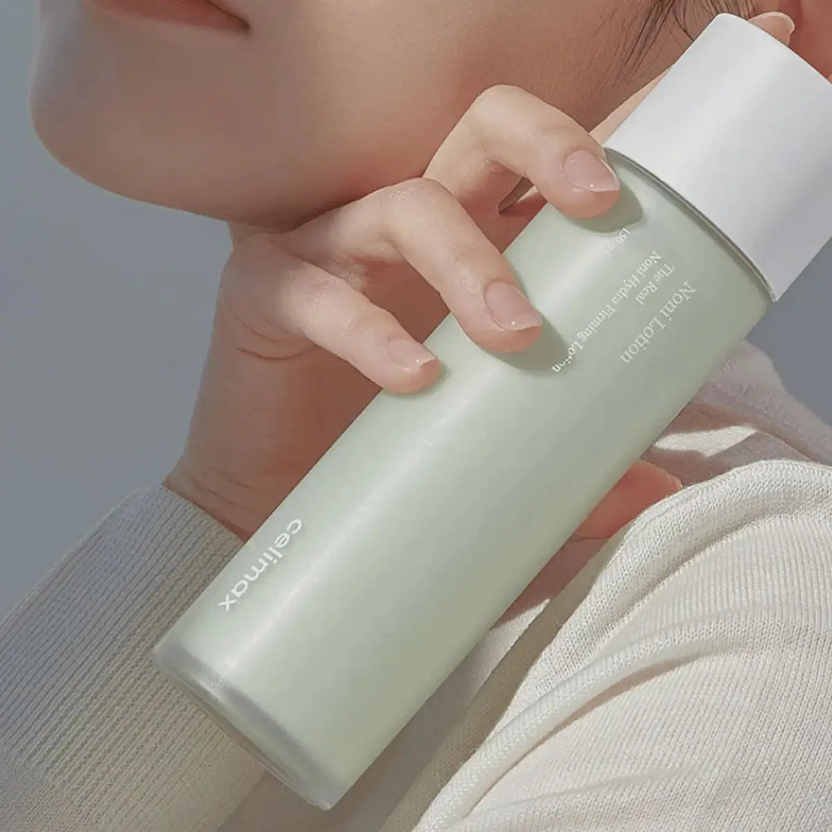 Person holding a light green bottle with a white cap, featuring the brand 'Cermax'.