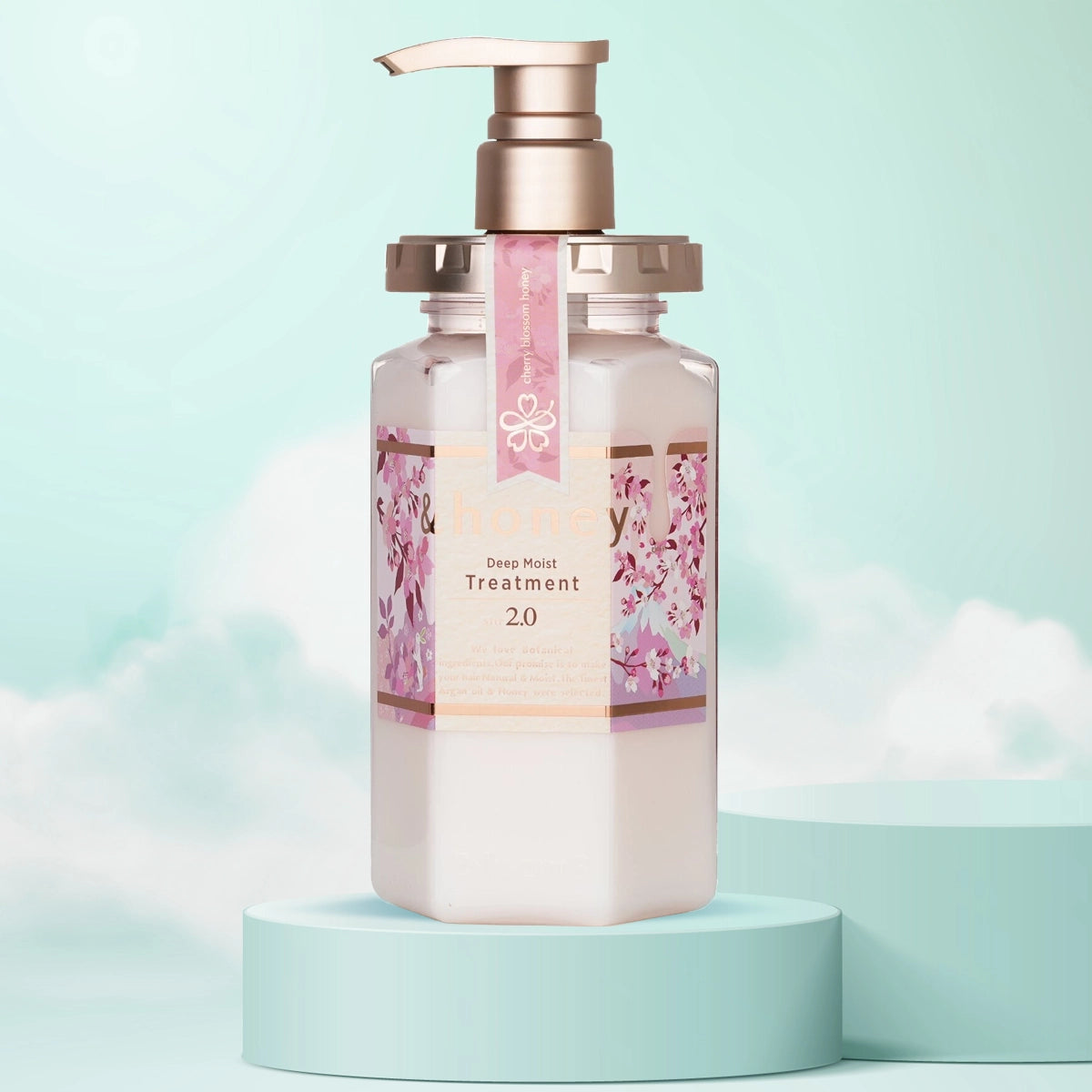 A pump bottle of &Honey Deep Moist Cherry Blossom Honey Treatment with floral designs on the label, presented on a teal platform with a light blue background.