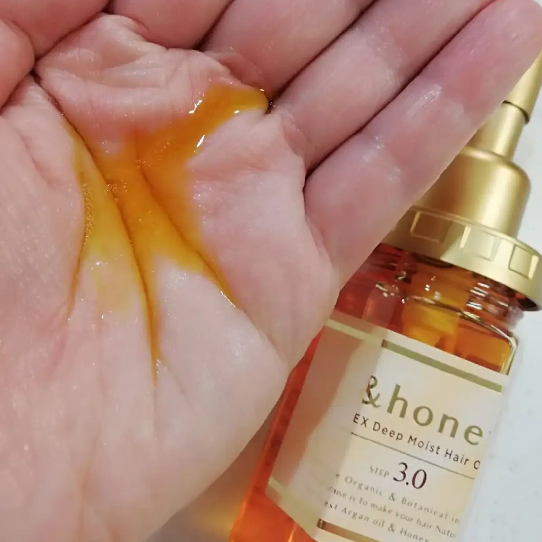 &Honey EX Deep Moist Hair Oil 100mL poured into a hand, showcasing its luxurious texture and shine.
