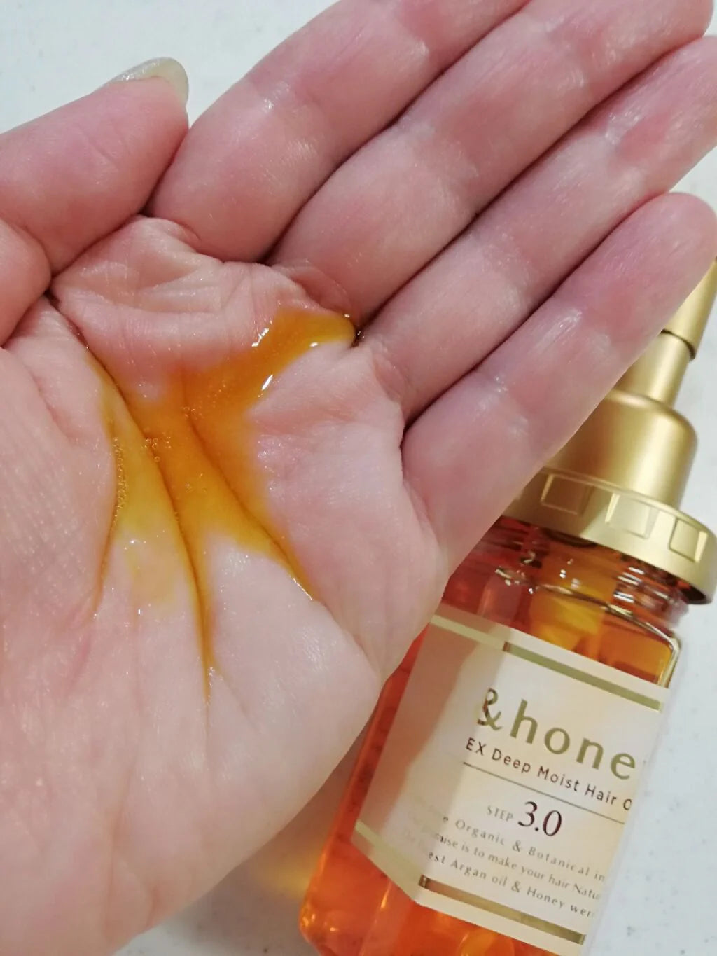 Hand holding a bottle of ViCREA &Honey EX Deep Moist Hair Oil – nourishing Japanese hair oil with honey blend for silky, with a pump dispenser.