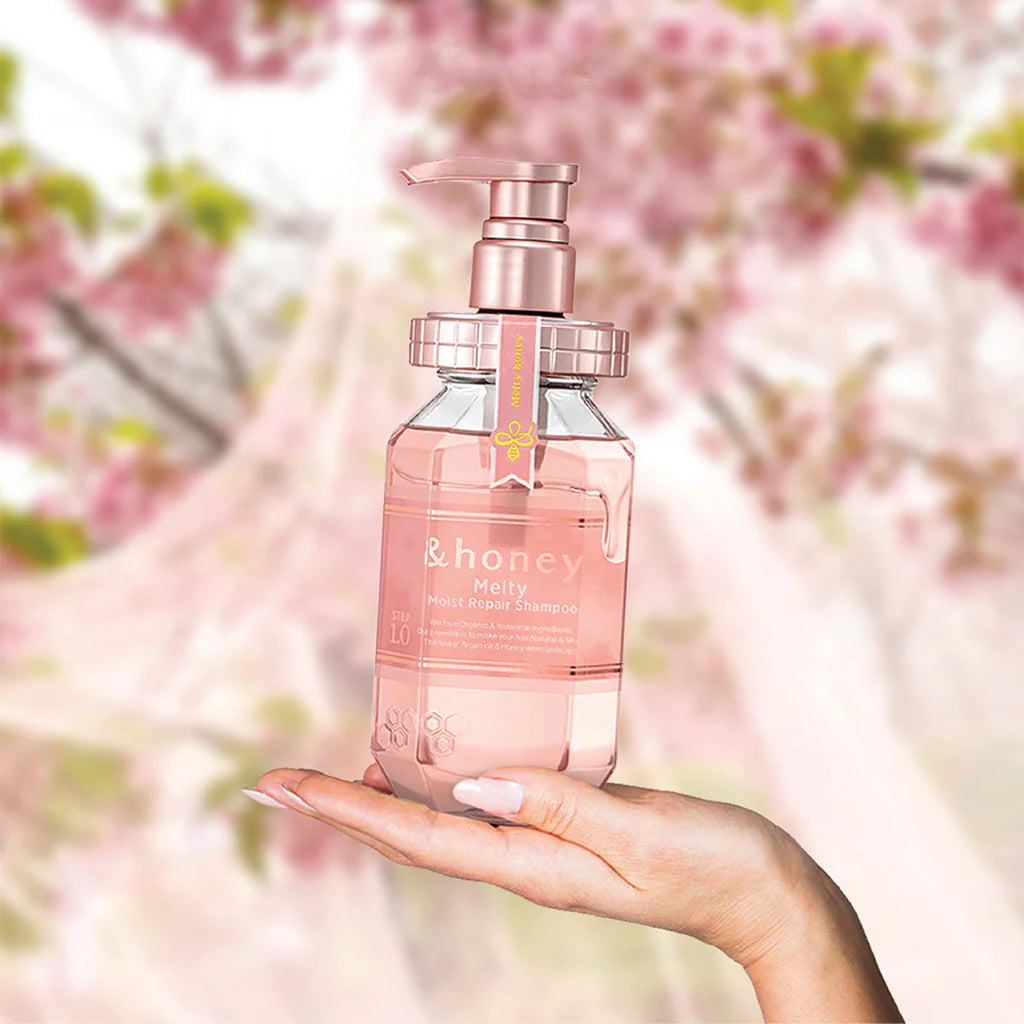 Hand holding a pink bottle of shampoo with a cherry blossom background.