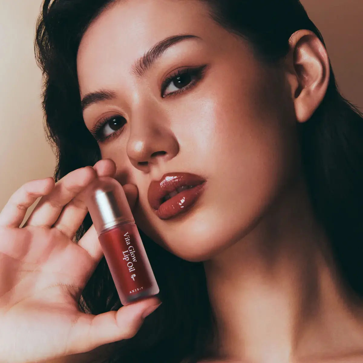 Woman holding a lip oil product close to her face