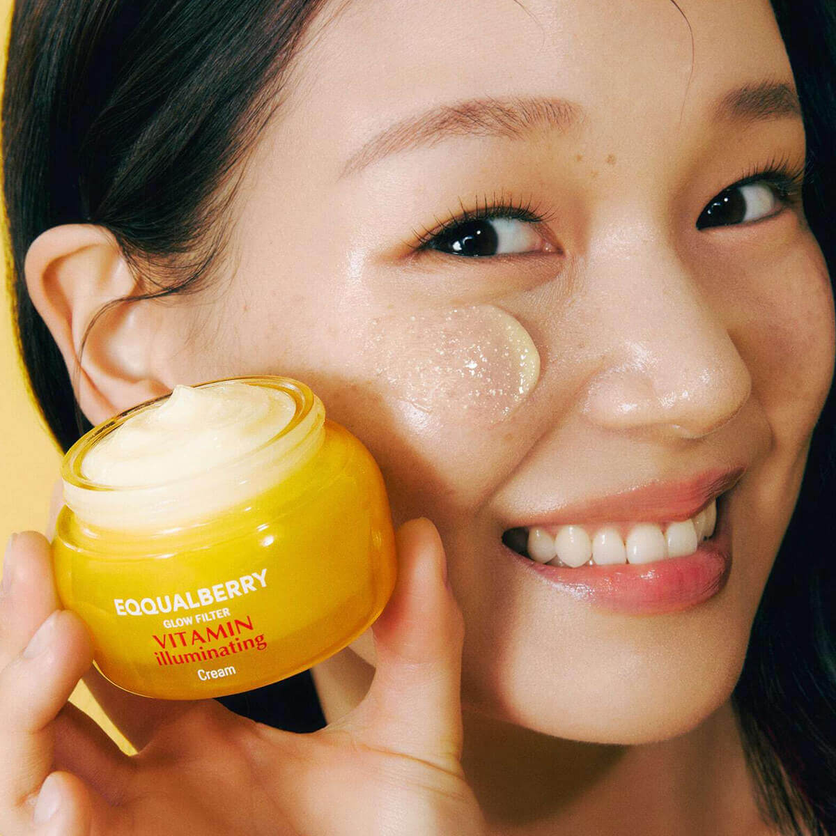 Vitamin Illuminating Cream in a yellow jar held by a smiling woman, showcasing its brightening skincare benefits.