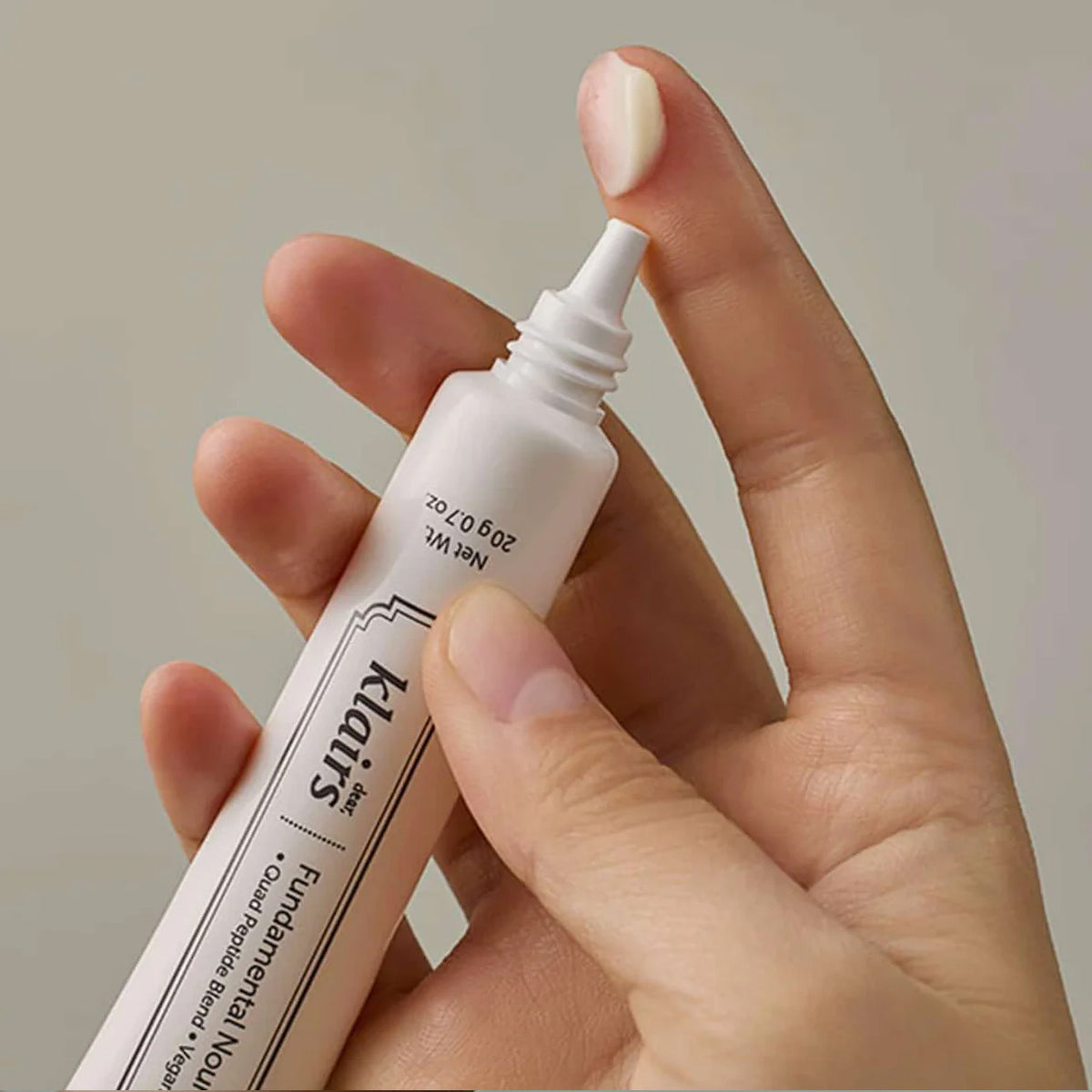 Hand holding a dear Klairs Fundamental Eye Cream against a neutral background