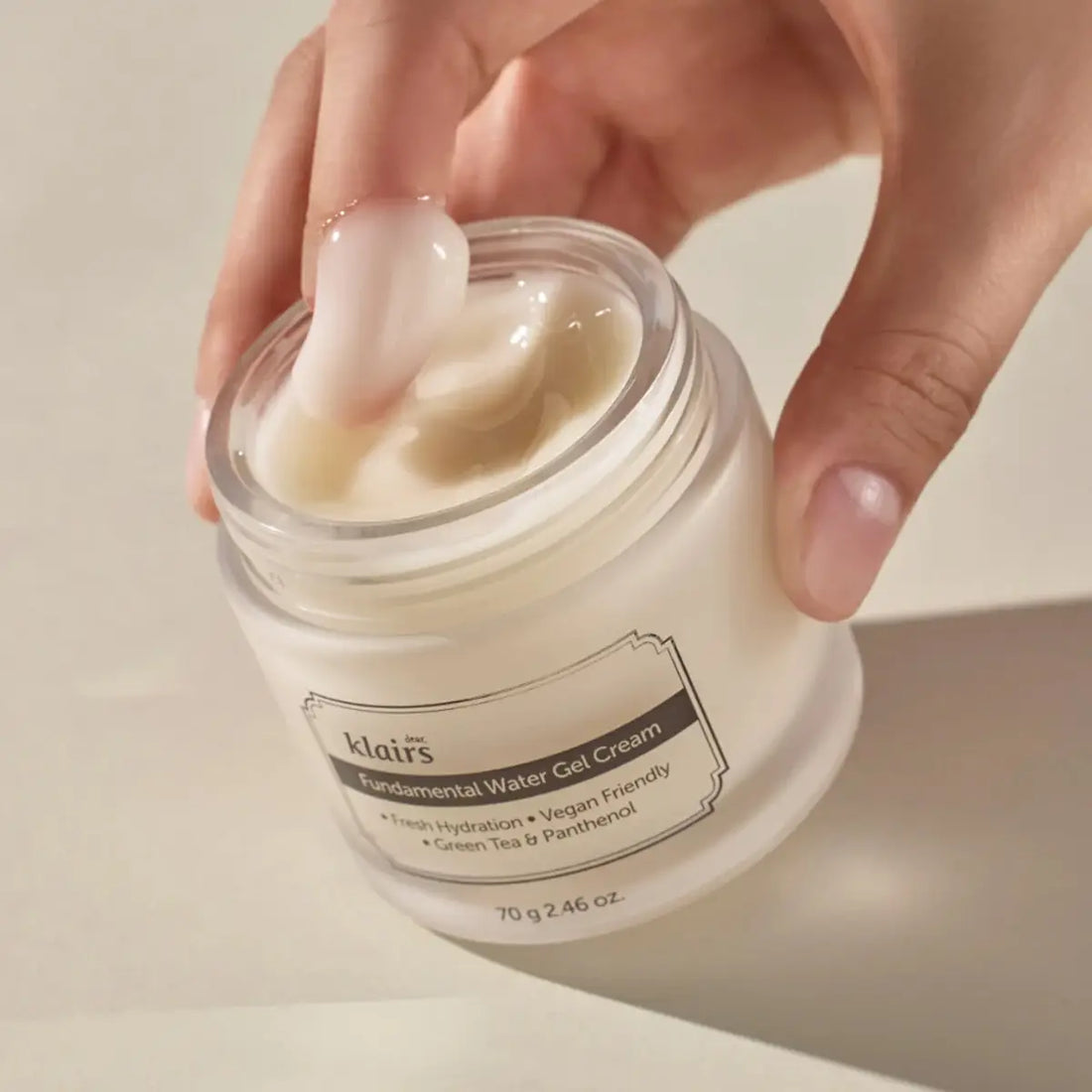 Hand holding a jar of Klairs Fundamental Water Gel Cream with visible cream on a neutral background
