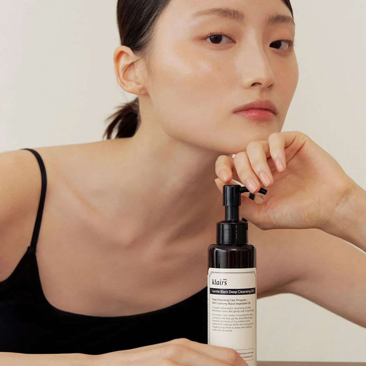 Woman holding a bottle of dear Klairs skincare product against a neutral background