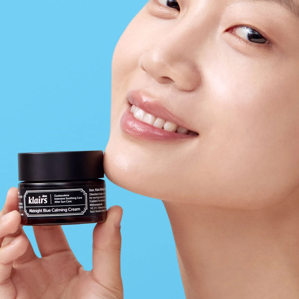 Person holding a jar of Klairs cream against a blue background