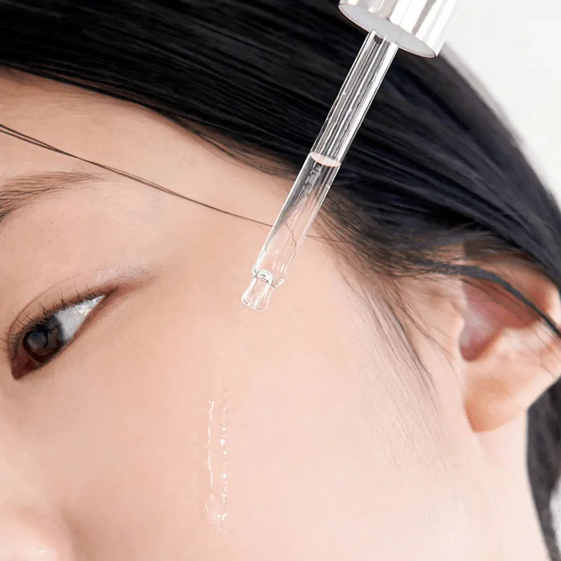 Close-up of a dropper applying serum on face.