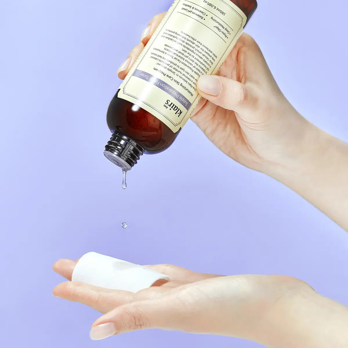 Hand holding a bottle of dear KLAIRS Supple Preparation Facial Toner droplet falling onto another hand against a light purple background