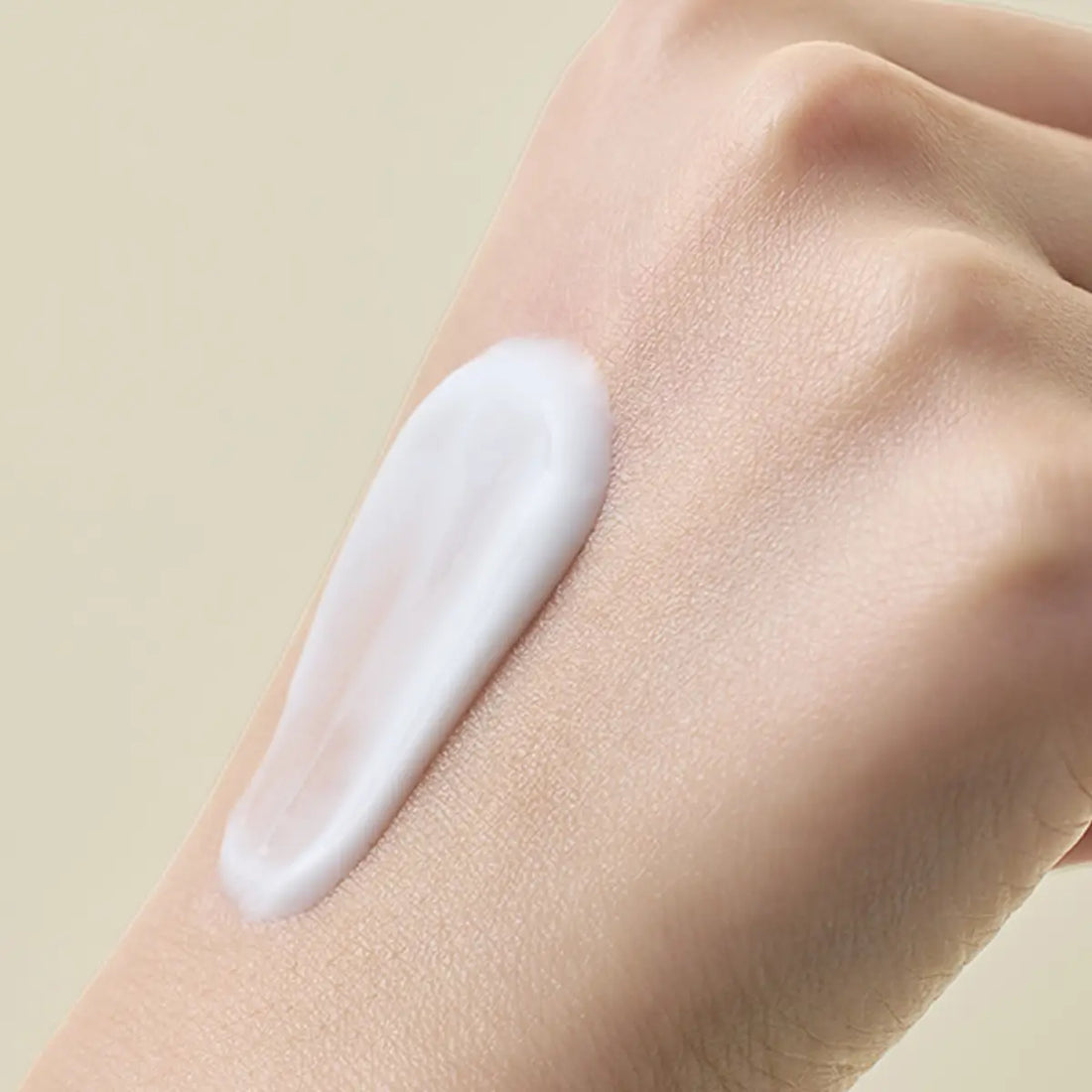 Hand with a white cream application on a beige background