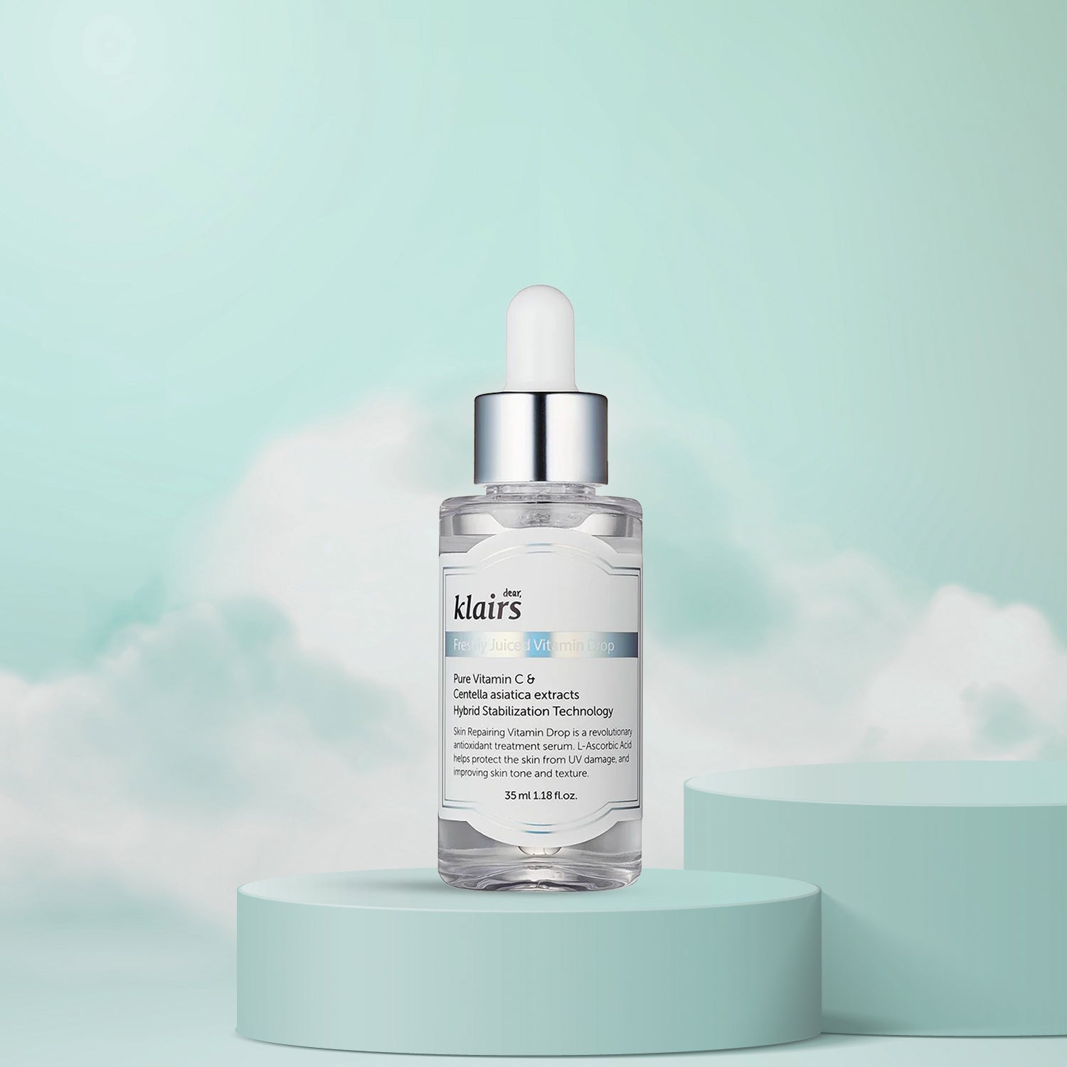 A bottle of dear KLAIRS Freshly Juiced Vitamin Drop serum on a pedestal against a cloud-filled sky background, showcasing the product label and dropper.