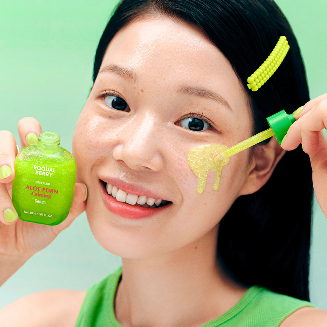 Woman applying Aloe PDRN Calming serum to her face with a green background