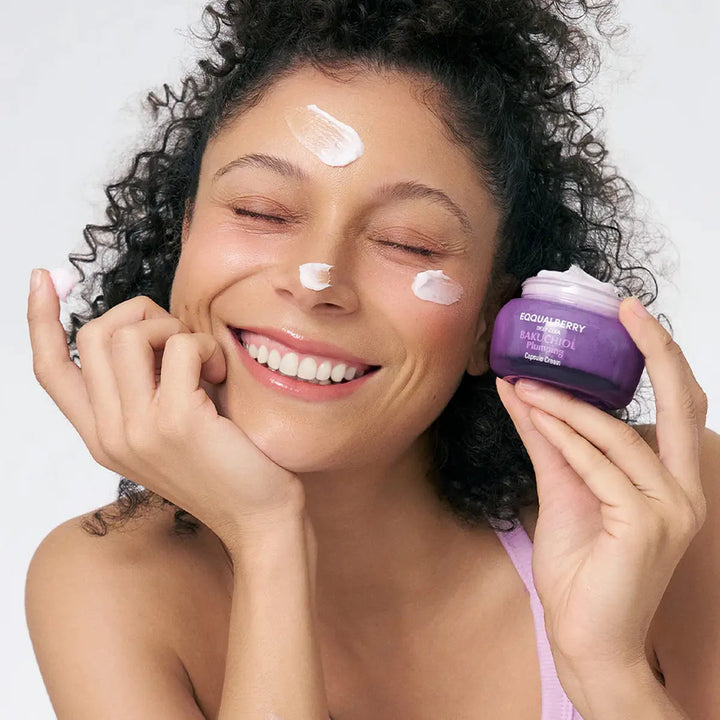 Woman applying cream to her face with a purple jar labeled 'Eqqualberry' on a white background