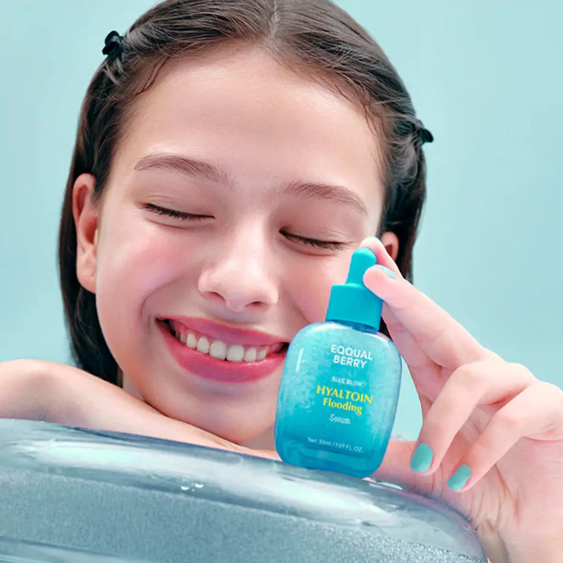 Girl holding a blue bottle labeled 'Eqqualberry' against a light blue background
