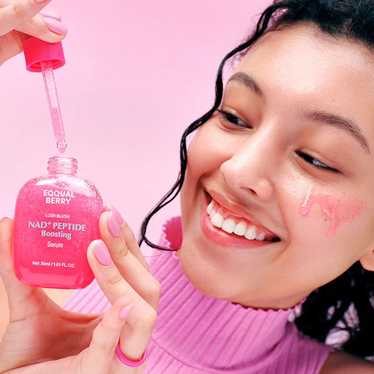 Person applying pink skincare serum to face with a dropper against a pink background